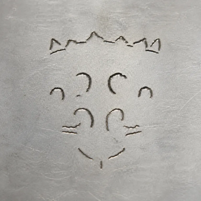 Henry Wilkinson & Co.: Deliberately unresolved compact device: broken crown-like upper points above sparse symmetric incomplete curled strokes and a faint downw…; oxidized reconstruction.