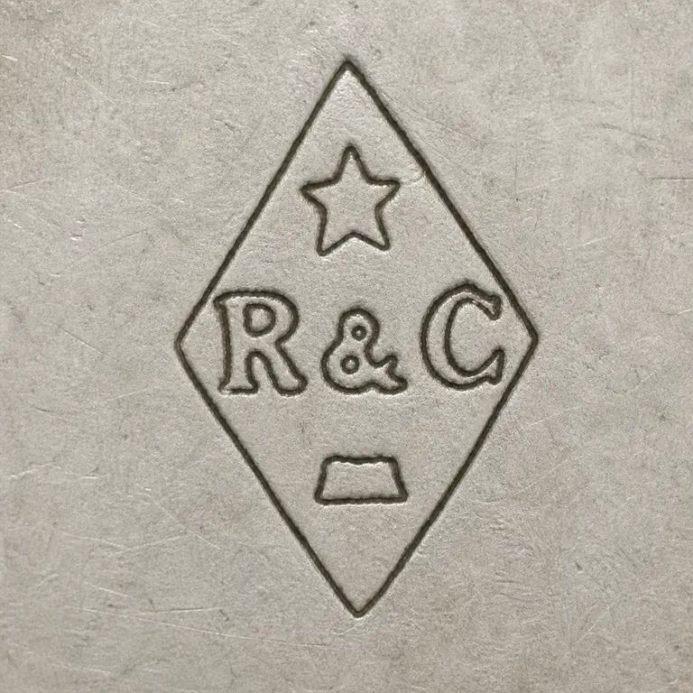 Rudolphe Beunke: A vertical diamond with one five-point star, the exact row R ampersand C, and one small worn trapezoid-like lower fragment; oxidized reconstruction.