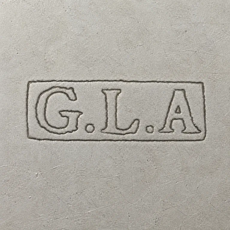 George Leonard Allen: G.L.A in worn uppercase letters with one period after G and one period after L, inside one narrow rectangular cartouche; oxidized reconstruction.