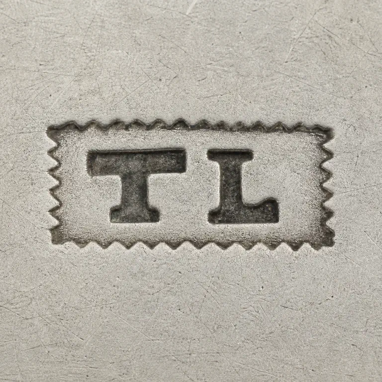 Thomas Law: TL as two bold uppercase capitals without punctuation, on one line inside one long narrow rectangular cartouche with serrated or notched…; oxidized reconstruction.