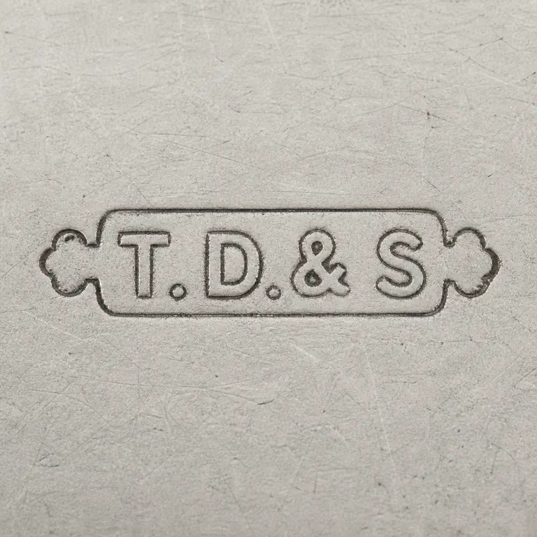 Thomas Ducrow & Sons: TD, ampersand, S, punctuation, plaque, and side ornaments in source order; oxidized reconstruction.