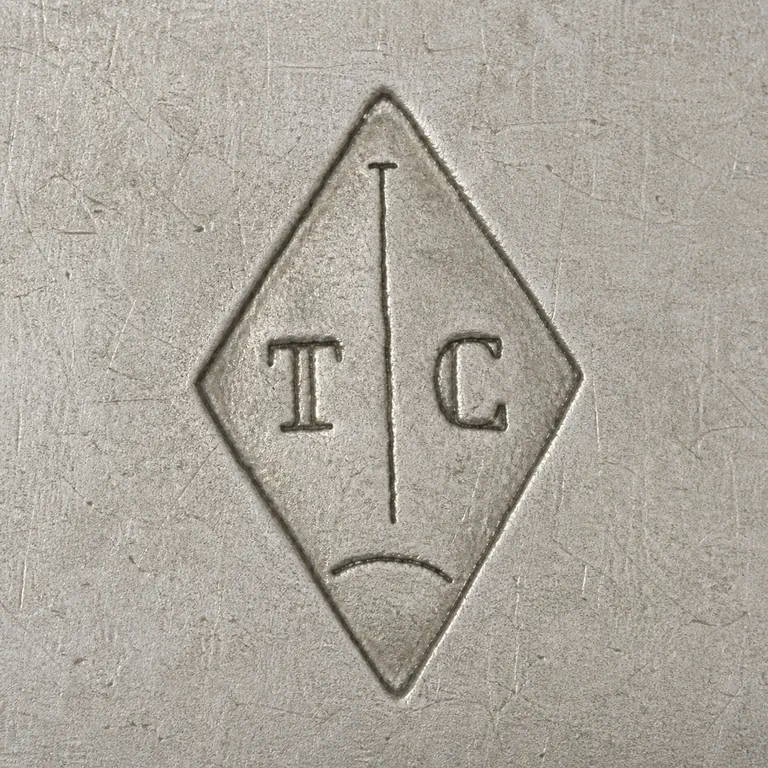 Tallois & Mayence: Vertical diamond with T at left, C at right, one plain central vertical line with a tiny top tick, and one separate shallow lower arc; oxidized reconstruction.