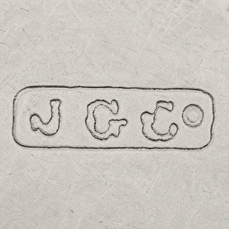 J G Co: Worn rounded plaque with J, G, ampersand-like, and Co-like forms; oxidized reconstruction.