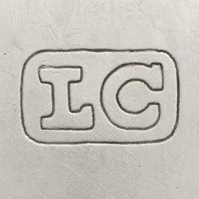 SILVERSMITH: Compact uppercase L C inside one rounded rectangular enclosure source's blunt, tightly spaced forms; oxidized reconstruction.