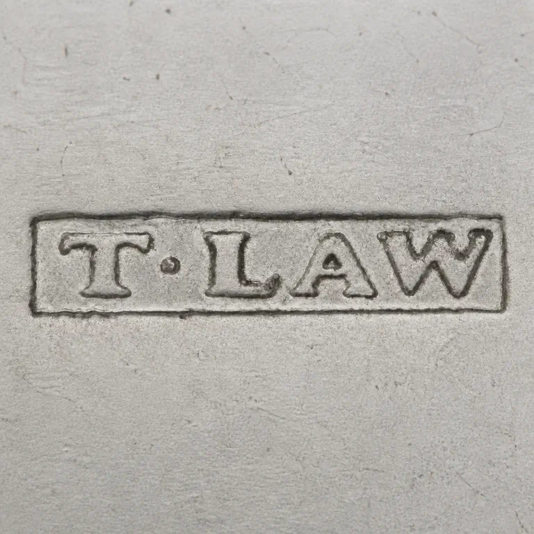 Thomas Law: T·LAW as uppercase T, one centered dot, then uppercase L, A, W on one line inside one long narrow rectangular cartouche; oxidized reconstruction.