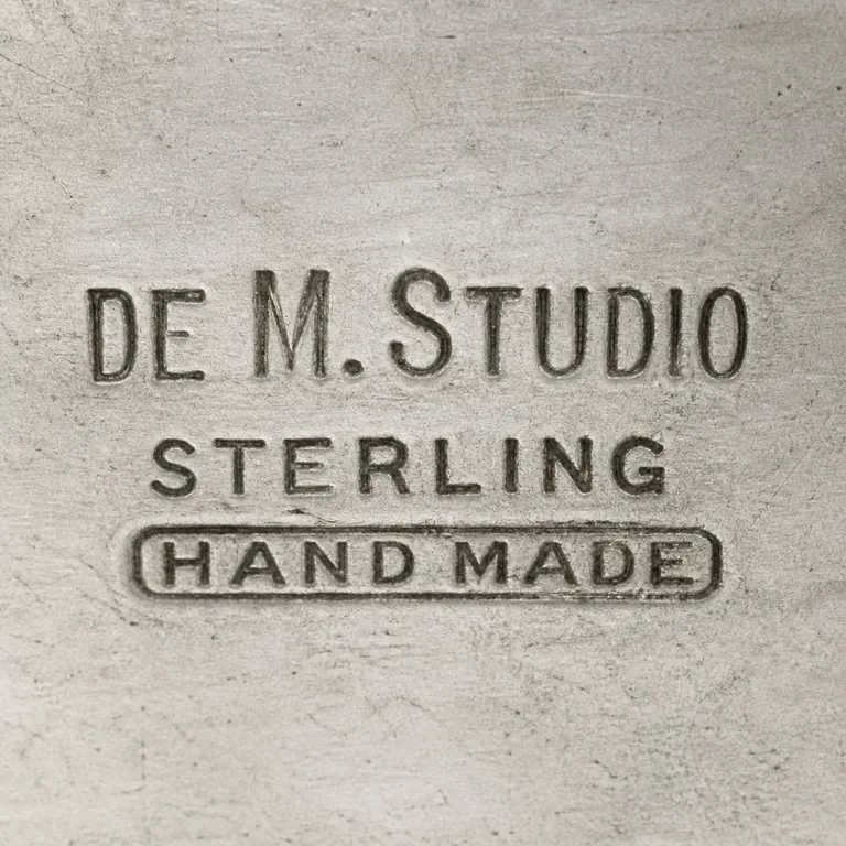 William G. DeMatteo (1895-1980): DE M. STUDIO, STERLING, and HAND MADE remain in the observed three-line composition; oxidized reconstruction.