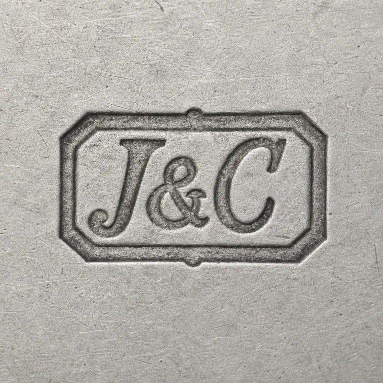 Jamieson & Carry: The ornate clipped-corner rectangular cartouche, inner border, J-like left form, ampersand, and C-like right form in order; oxidized reconstruction.