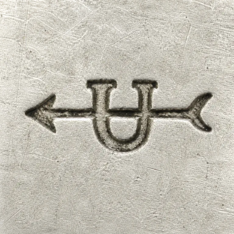 Uncas Mfg. Co.: A bold U-like shape is crossed by a long arrow-like shaft with pointed left and split right ends; oxidized reconstruction.