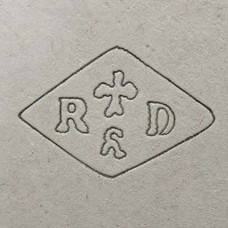 Rudolphe Beunke: Horizontal diamond enclosing R at left, D at right, a small worn fleur-like upper central device, and a smaller curled lower device; oxidized reconstruction.