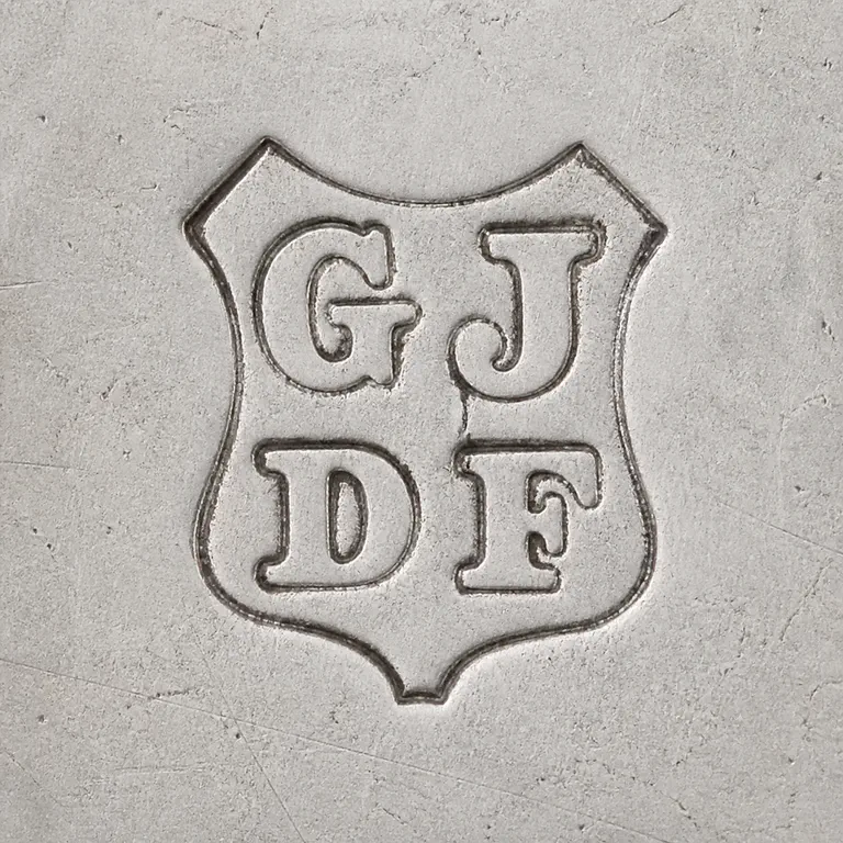 Josiah Williams & Co (George Maudsley Jackson & David Landsborough…: Preserves the ornate shield-like outer silhouette, two-by-two arrangement of G/J-like upper and D/F-like lower forms, and overall orienta…; oxidized reconstruction.