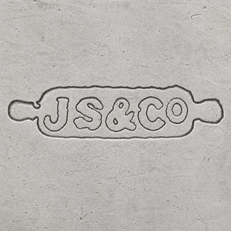 J S & Co: Long irregular capsule-shaped plaque with JS, ampersand-like central mark, and CO sequence; oxidized reconstruction.