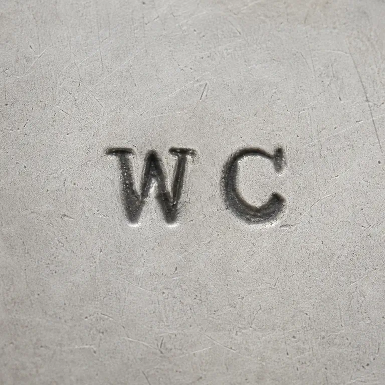 William Chinn: Unenclosed W and C forms are reconstructed side by side in the source reading direction with no invented plaque or ornament; oxidized reconstruction.