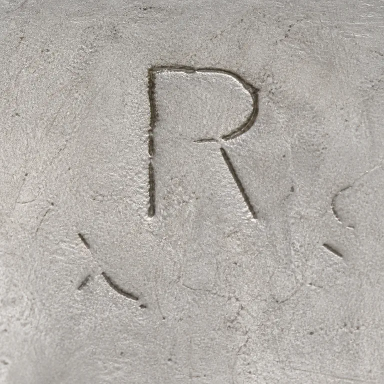 Raimond Silver Mfg. Co.: One large R is readable; only fragmentary curved and short strokes are visible nearby; oxidized reconstruction.