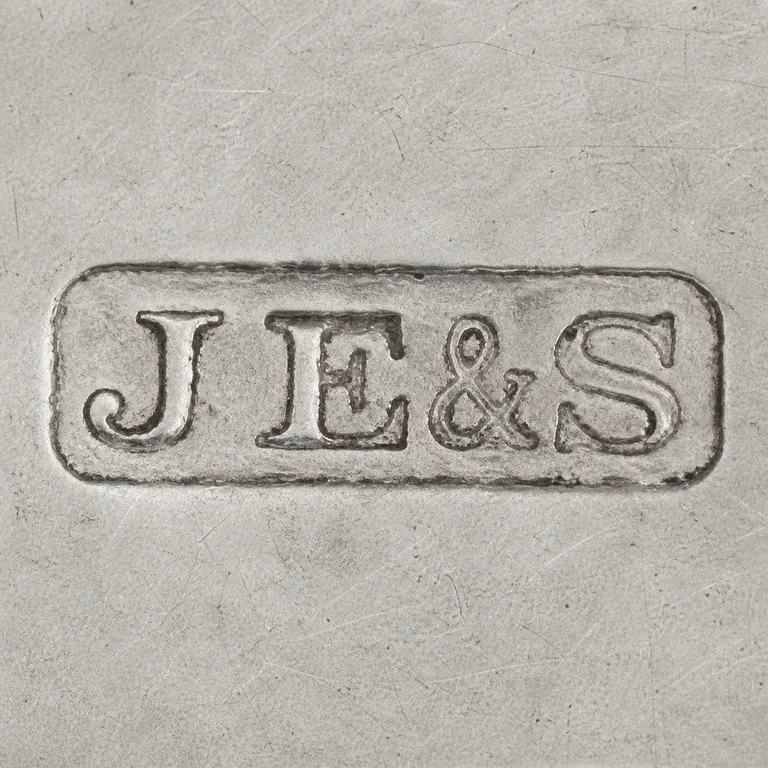 John Eldridge & Sons Sterling Inkwell 1915 London: Uppercase J, uppercase E, ampersand, and uppercase S inside one long horizontal rounded-rectangle cartouche; oxidized reconstruction.