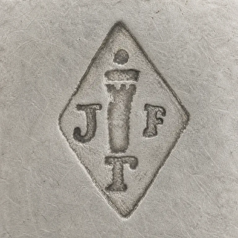 Joseph Antoine: Vertical diamond with J left, F right, T bottom, a tall central column-like device, and a small upper dot and cap; oxidized reconstruction.