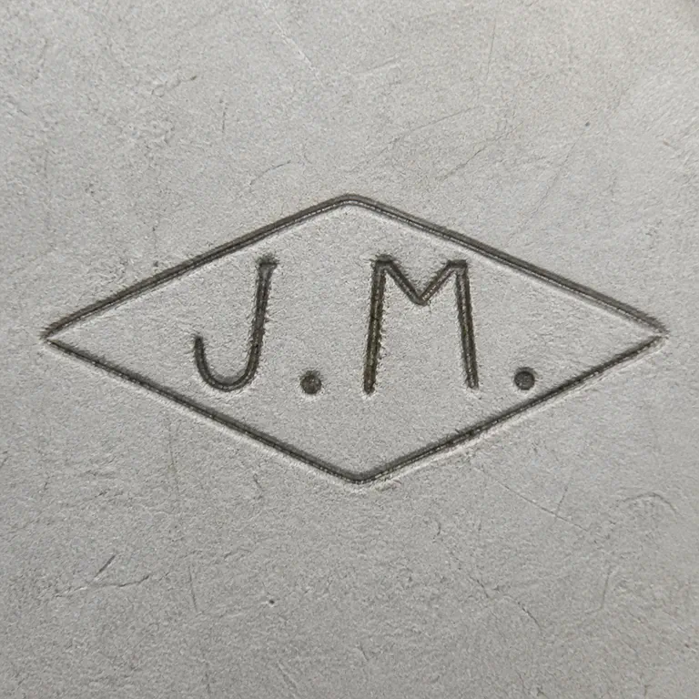 J M: A pointed diamond punch with J.M forms and punctuation is reconstructed enclosing geometry; oxidized reconstruction.