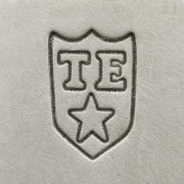 T E, mullet below: T E arranged inside one shield-shaped enclosure with a detached star-like element below; oxidized reconstruction.
