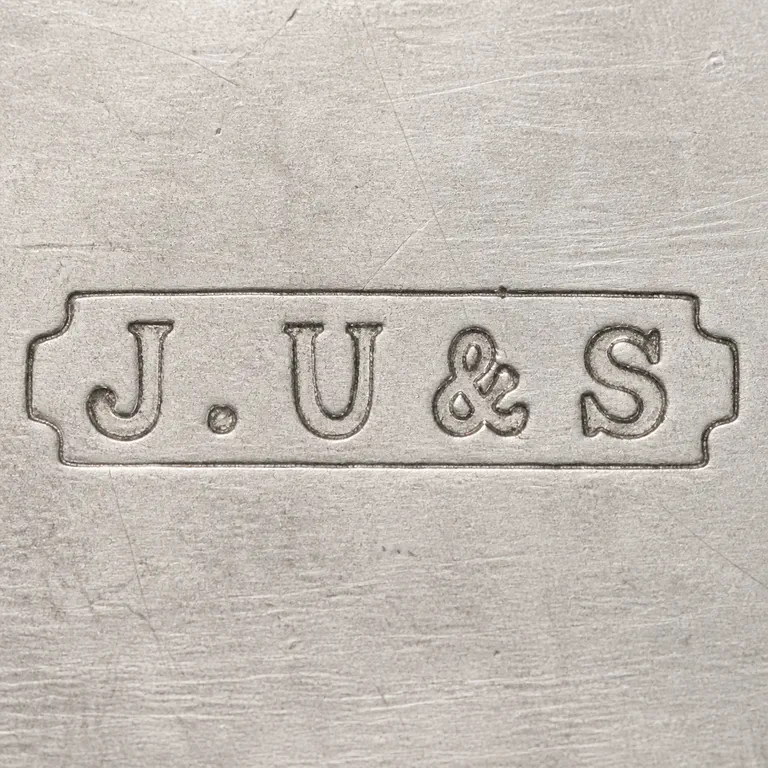 James Usher & Son: J.U&S as uppercase J, one dot, uppercase U, ampersand, and uppercase S on one line inside one long narrow rectangular cartouche with smal…; oxidized reconstruction.