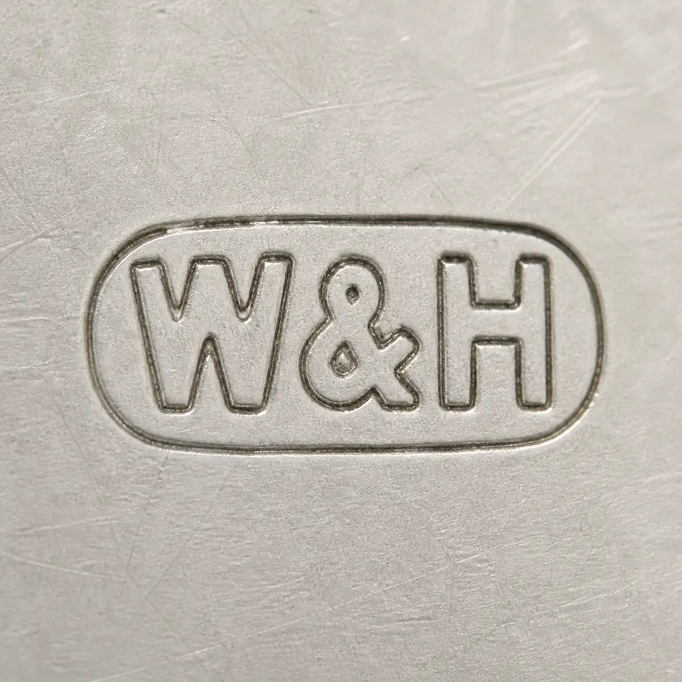 Walker & Hall: W&H as uppercase W, one ampersand, and uppercase H on one line inside one horizontal oval or capsule cartouche; oxidized reconstruction.