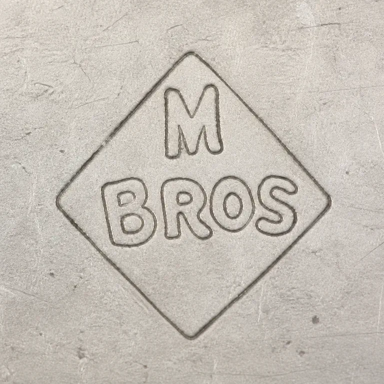 Mappin Brothers: Uppercase M centered on the upper tier above the uppercase word BROS on the lower tier, all inside one diamond-shaped cartouche; oxidized reconstruction.