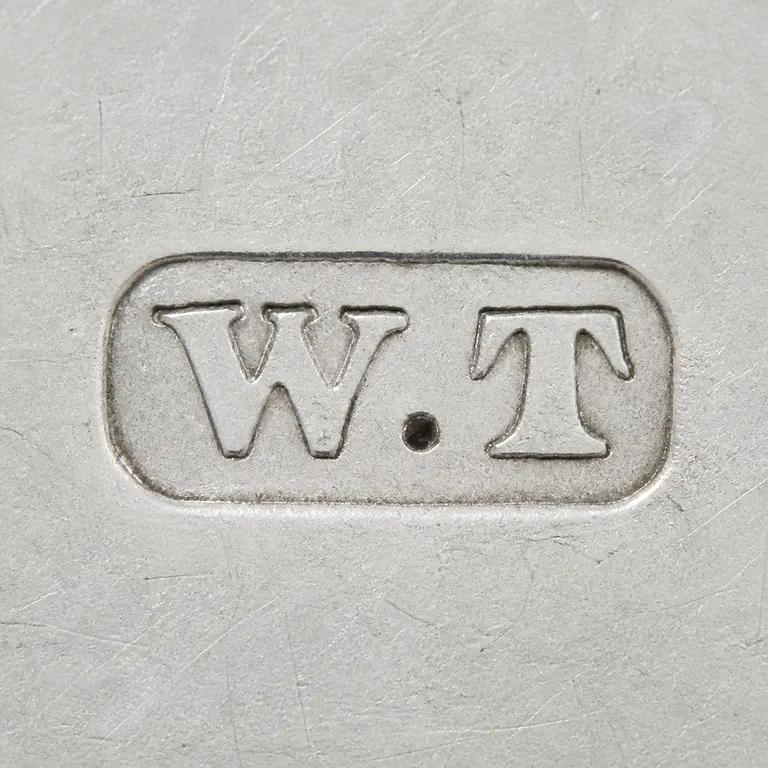 Walter Trickett: Uppercase W, one centered dot, then uppercase T on one line inside one compact rounded-rectangle cartouche; oxidized reconstruction.