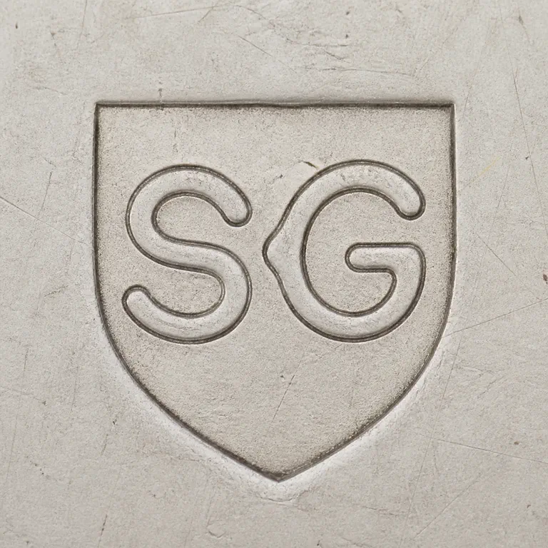Stanley Glass: Pointed shield-like border with S-like and G-like interior forms, upright and centered; oxidized reconstruction.