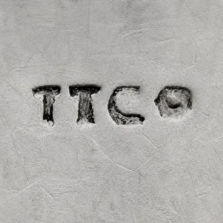 T T Co: The T, T, C, and small final rounded character are retained in order with their separated spacing and worn serif-like contours; oxidized reconstruction.